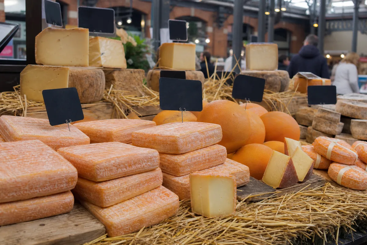 Étal de fromager sur un marché couvert du Nord présentant Maroilles, Mimolette et fromages à croûte orange