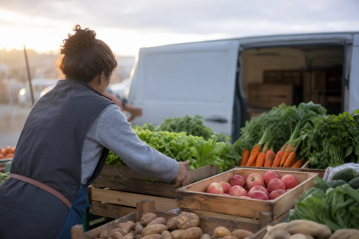 Vendeuse installant un étal de fruits et légumes tôt le matin sur un marché de plein vent