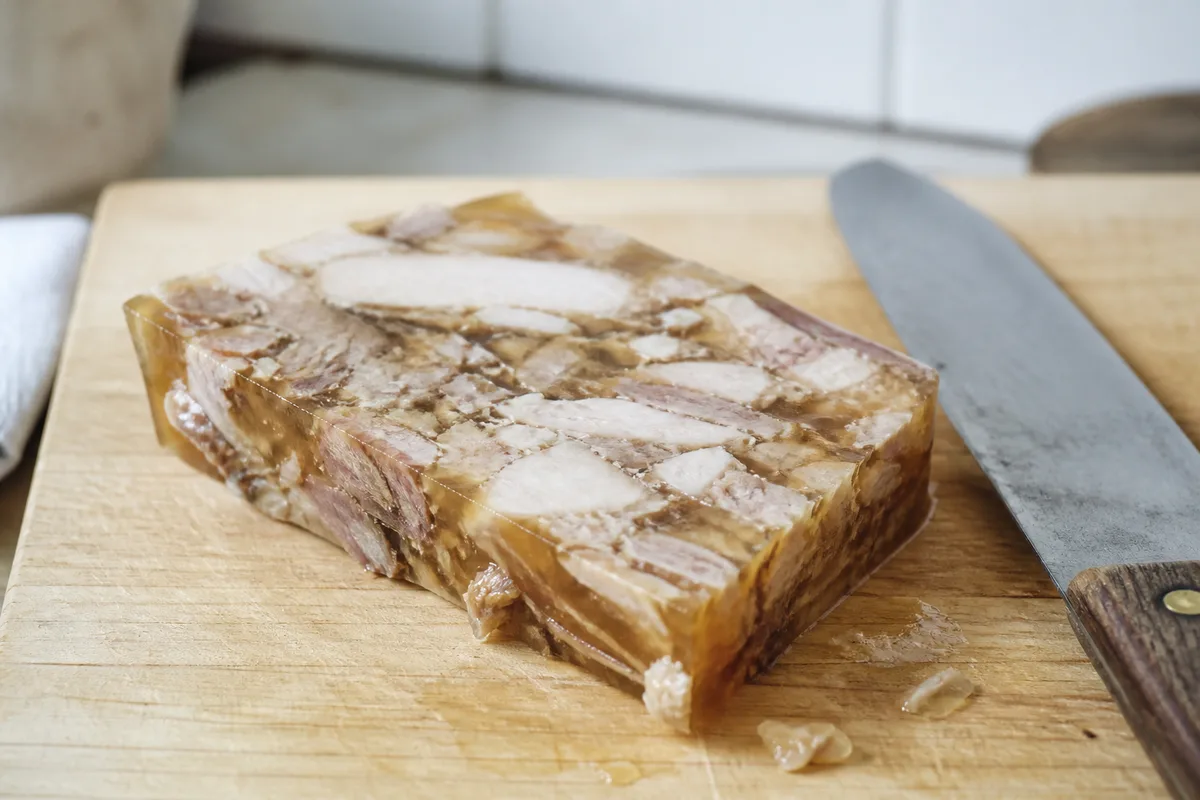 Terrine de potjevleesch tranchée sur une table en bois dans une cuisine flamande